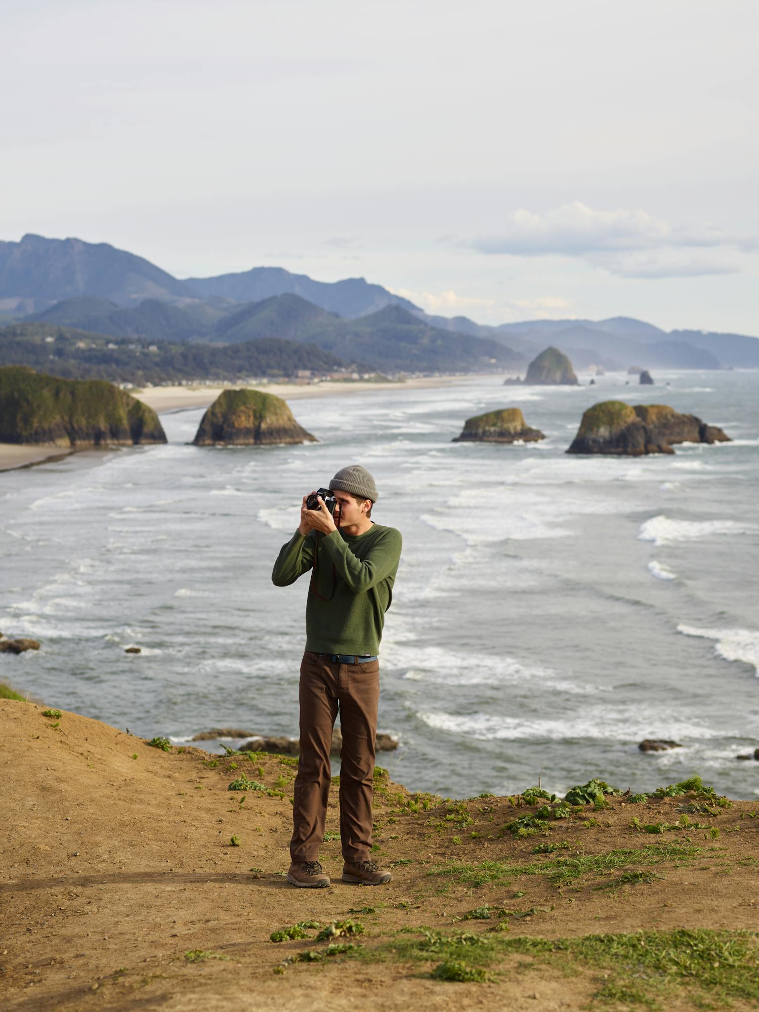 High angle of young male photographer in casual clothes standing on rocky viewpoint and taking pictures of amazing landscape with camera